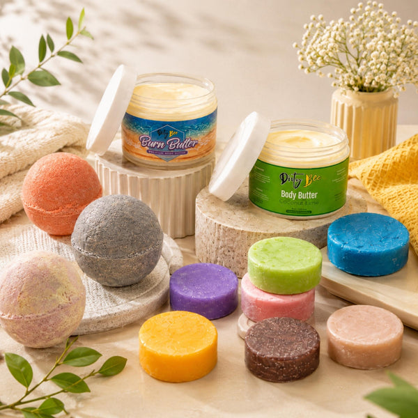 Dirty Bee body butters, bath bombs, and colorful solid hair bars arranged in a bright spa-inspired setting with towels, flowers, and greenery.