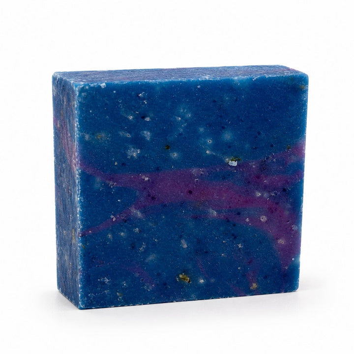 Dirty Bee Cosmic Soap Bar, a square deep blue bar with purple marbling and metallic flecks, on a white background.