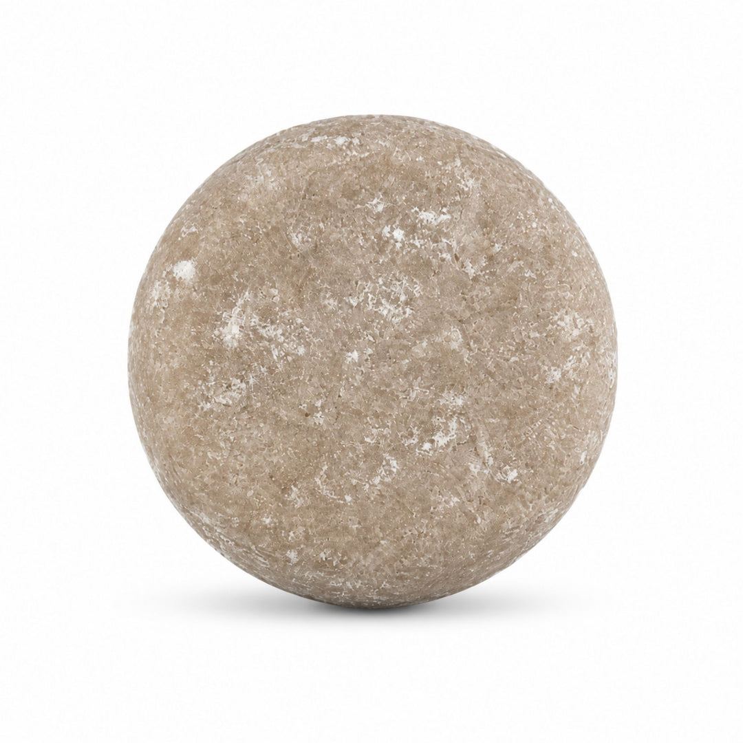 Dirty Bee Honey Almond Shampoo Bar, a round beige and gray textured shampoo bar, on a white background.