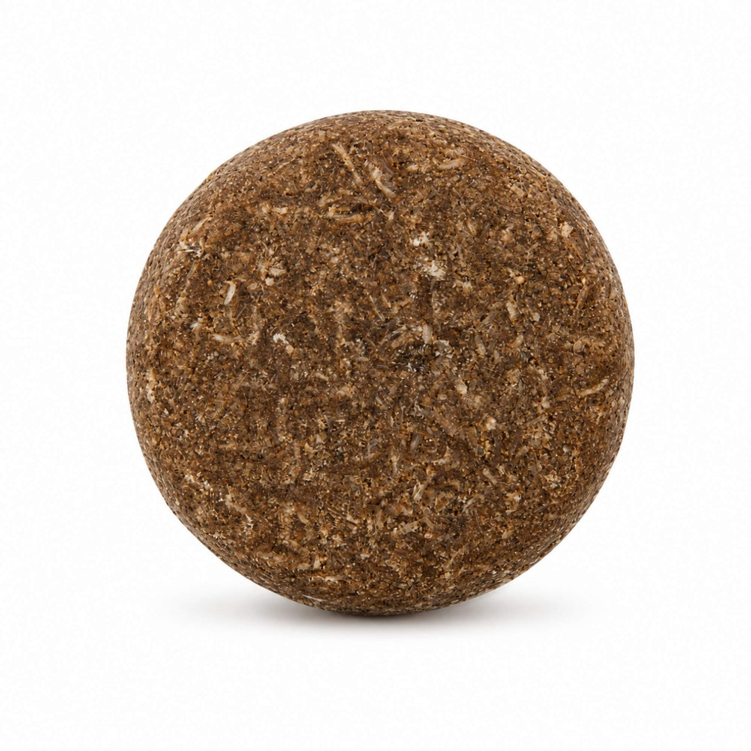 Dirty Bee Keeper Shampoo Bar, a round textured brown shampoo bar with a granular surface, on a white background.