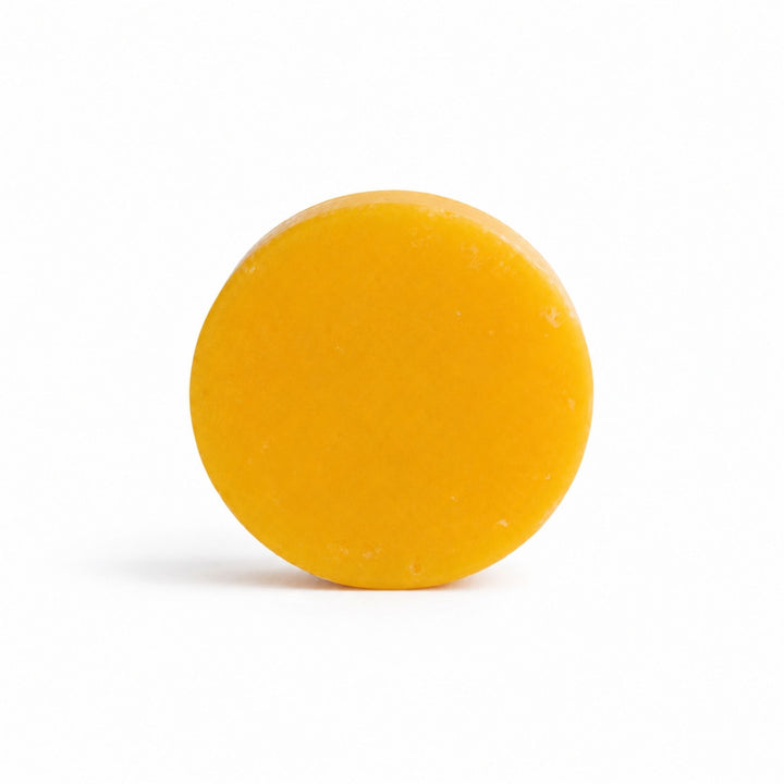 Dirty Bee Pineapple Mango Conditioner Bar, a round golden yellow solid bar on a clean white background.