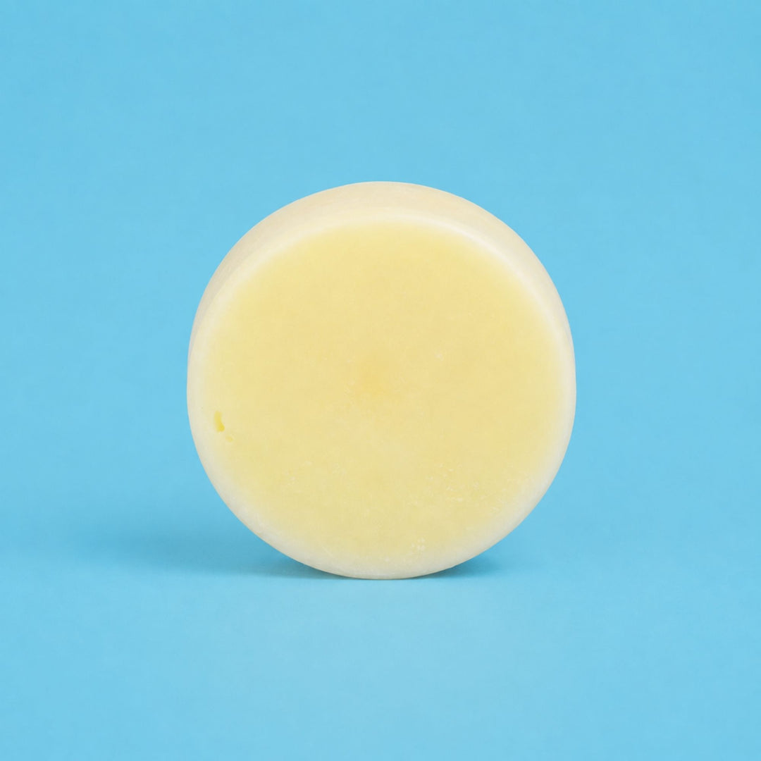 Dirty Bee Strengthen Conditioner Bar, a round pale yellow solid bar on a light blue background.