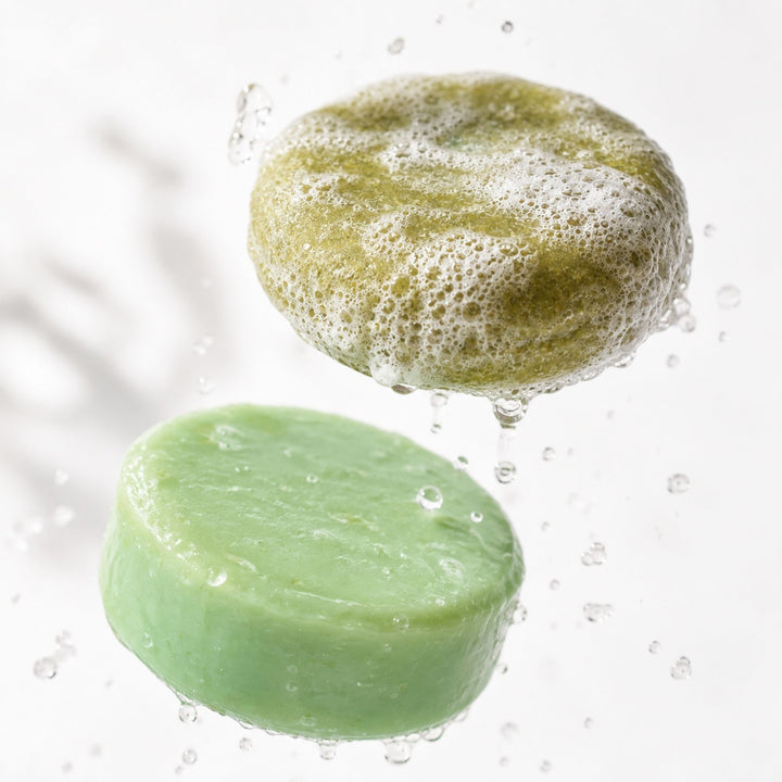 Dirty Bee Coconut Lime Shampoo Bar and Conditioner Bar floating with water droplets and rich lather on a bright white background.