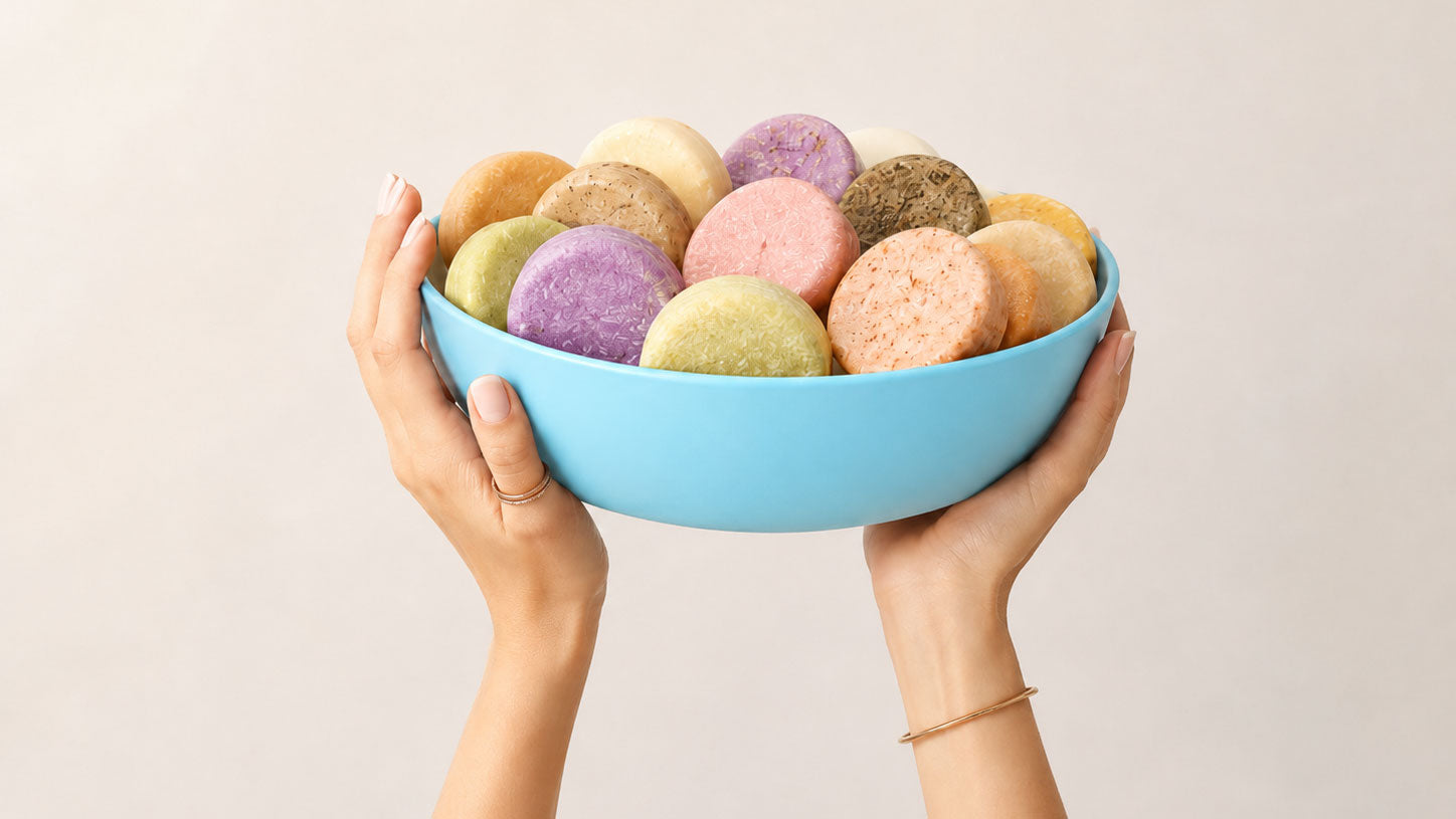 Hands holding a light blue bowl filled with assorted colorful conditioner bars.